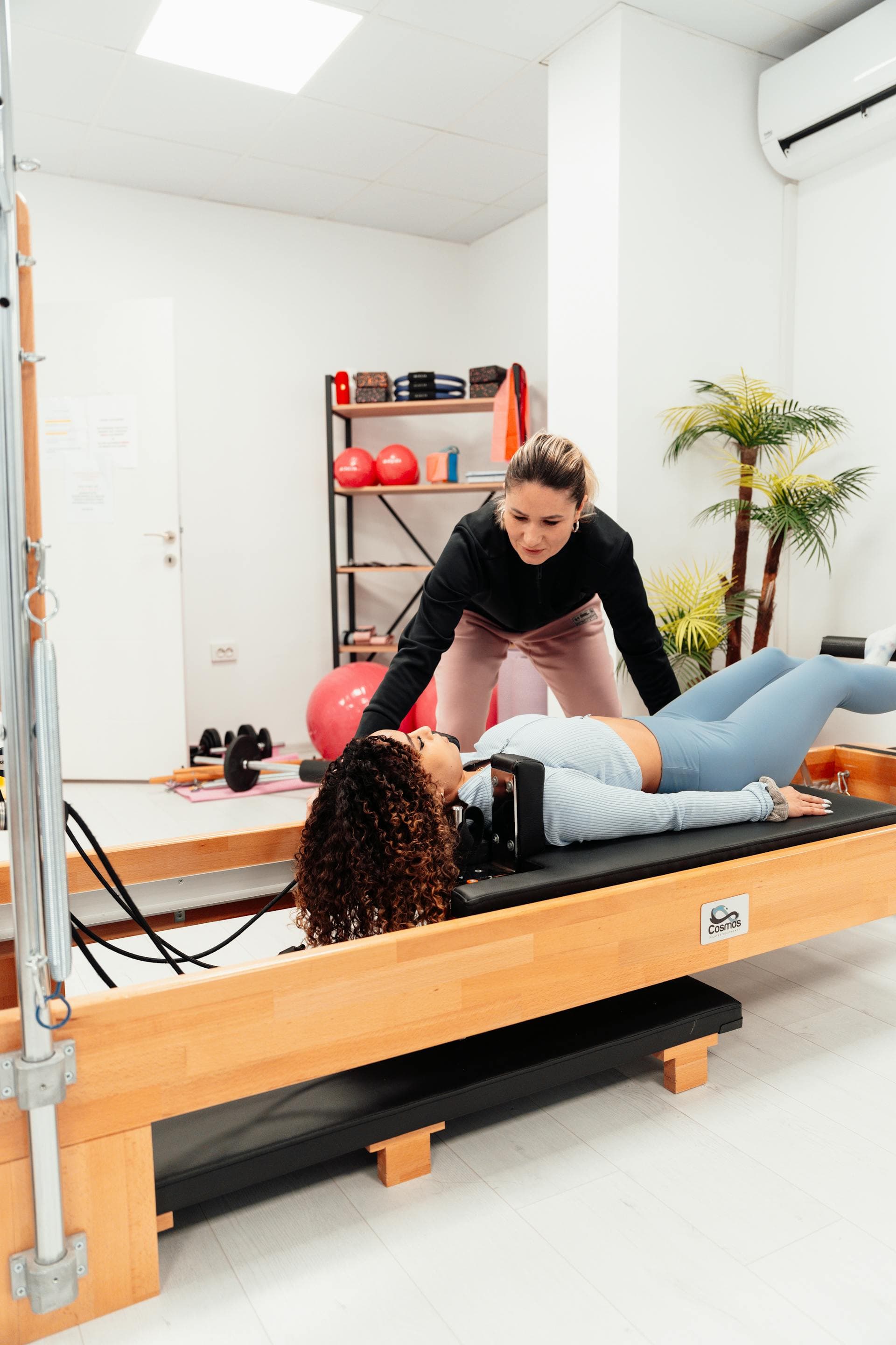Instructora corrigiendo a alumna tumbada en máquina Reformer en Aura Pilates Studio, Barcelona